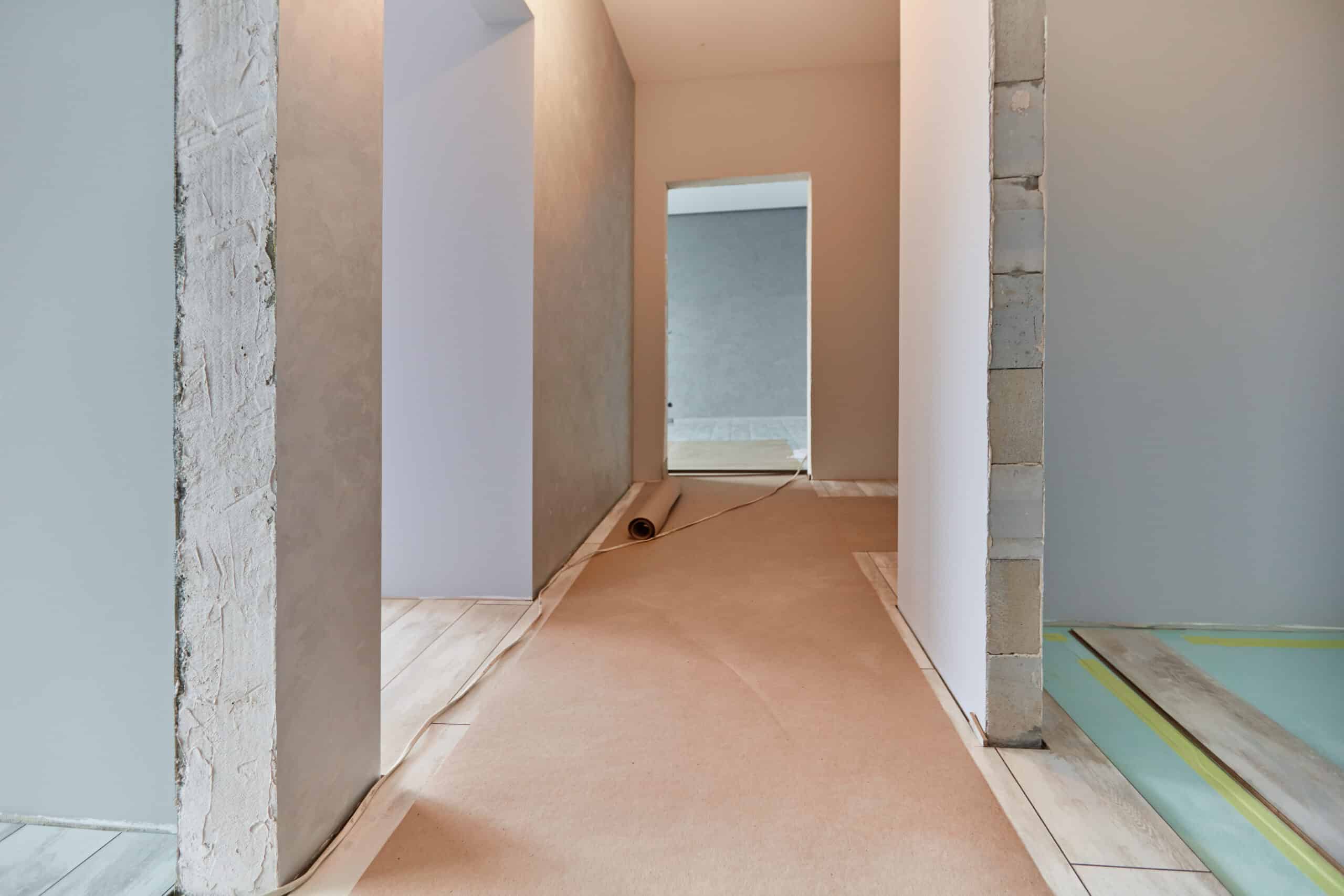 Couloir en rénovation avec sol protégé par papier kraft, des montants de mur bruts et des murs peints en attente de finitions.